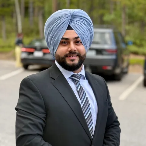Parmveer Baweja, smiling, in a dark suit and light blue turban
